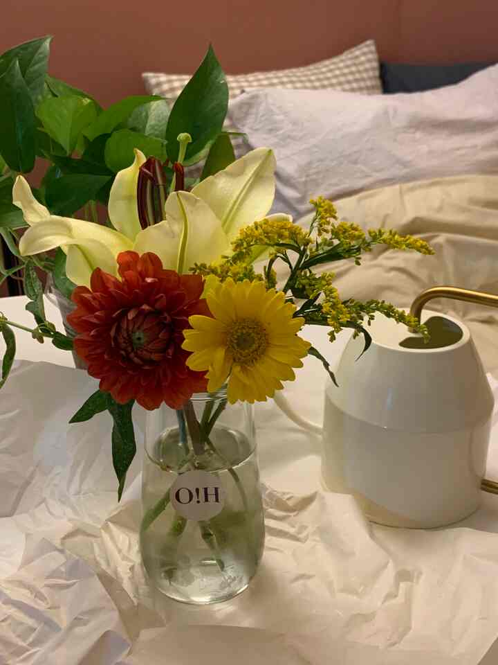 Warm brown-toned wall interior with a white table featuring a vase of colorful flowers and a watering can, creating a cozy plant display