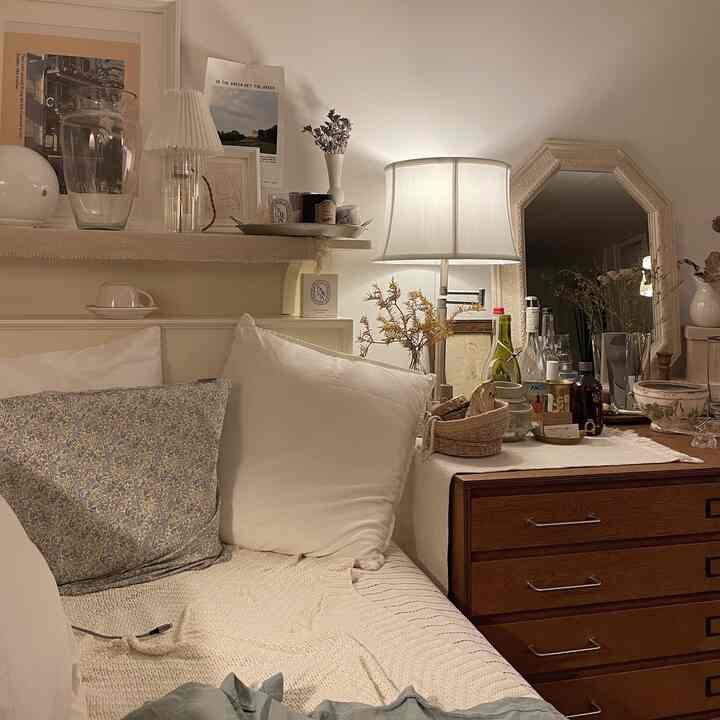 Soft white-toned bedroom-like living room featuring vintage wooden nightstand and table lamp with a cozy atmosphere