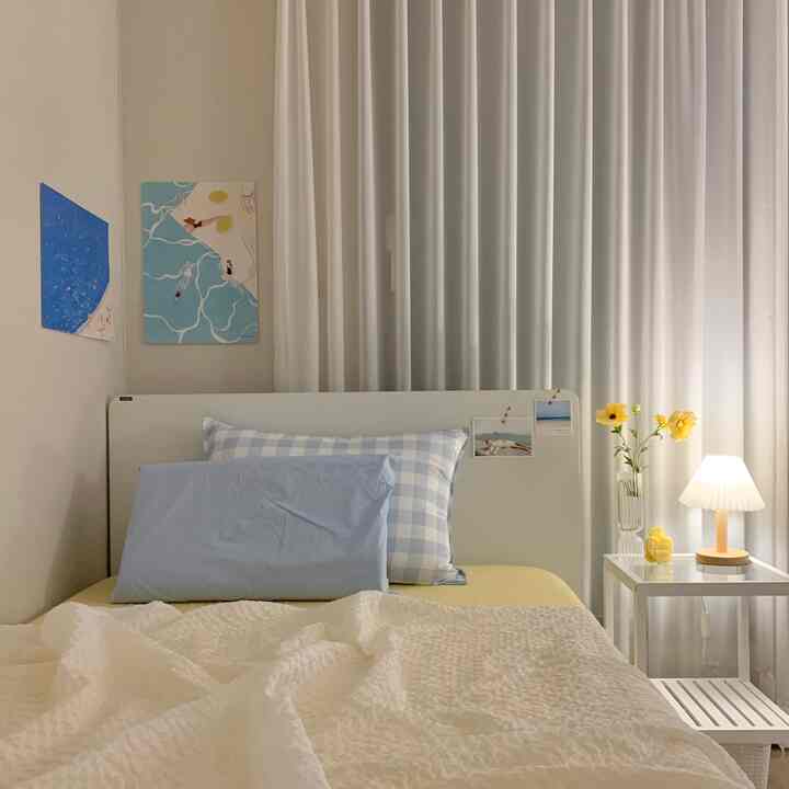 白と青のトーンの寝室、白い枕と青のチェック柄の枕が置かれたベッドとテーブルランプが配置された暖かな雰囲気のあるインテリア