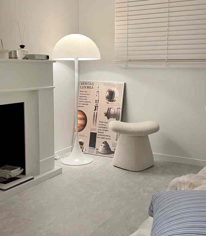 White-toned living room featuring a minimalist fireplace console, a distinctive white floor lamp, and a soft sculptural chair with a clean, minimal aesthetic