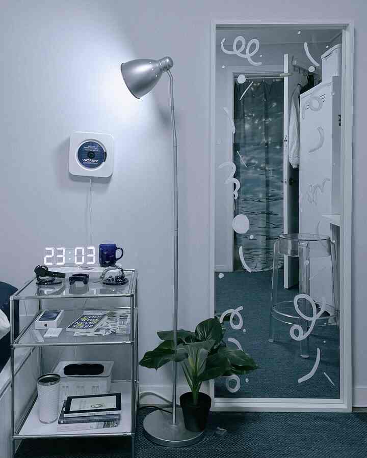 ホワイトとブルーのトーンの狭い部屋、フロアランプと大型の鏡、ガラスキャビネットが配置された印象的な空間