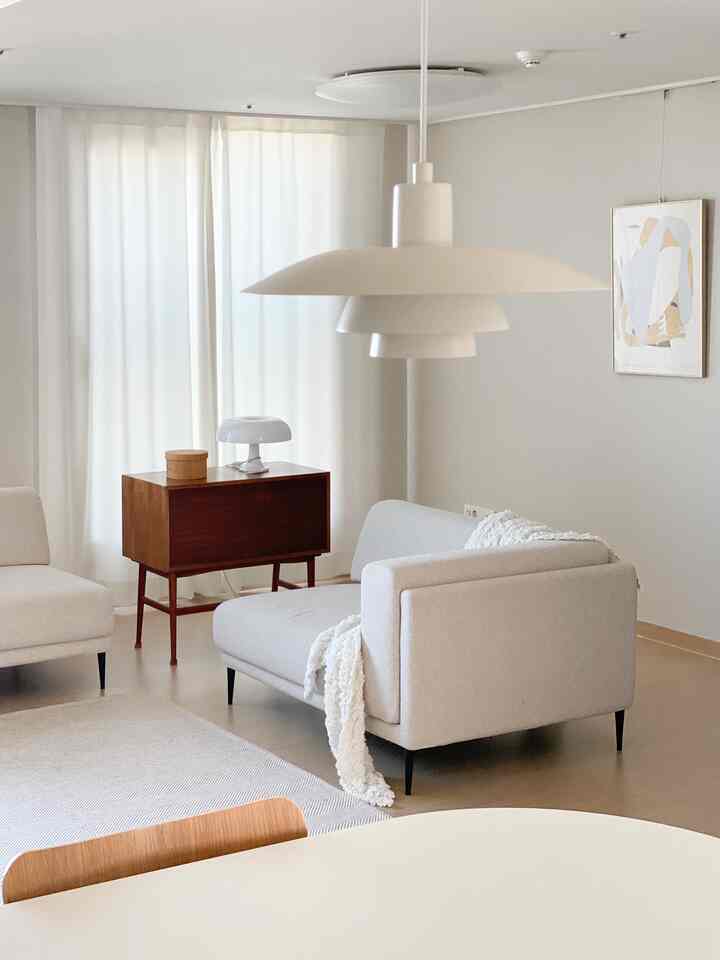Bright beige and white toned living room featuring fabric sofa, wood-tone console, and pendant light in a natural modern style