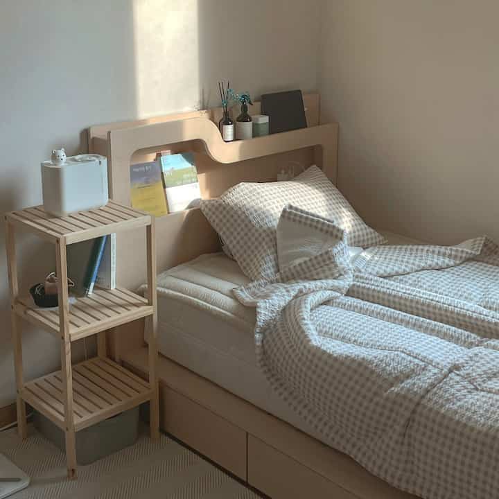 Cozy single bedroom with wood tone bed and beige check bedding illuminated by natural light