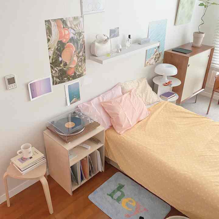 Natural tone bedroom with yellow bedding and pink pillows, posters and lighting create a warm cozy interior