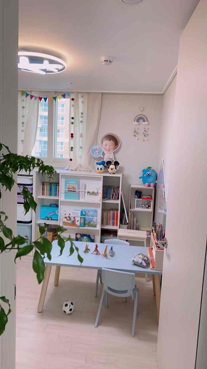 Soft white and light blue toned kids' room featuring a central desk and bookshelves in a cozy child-friendly space