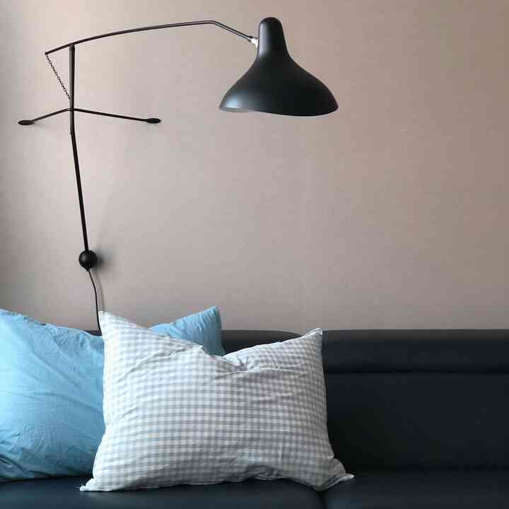 A modern living room featuring beige walls, a black sofa with blue and checkered pillows, and a black wall lamp