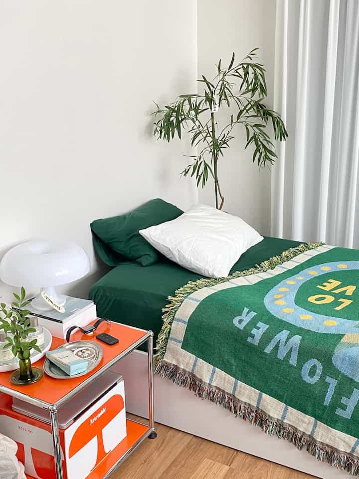 Cozy bedroom featuring green bedding and a nightstand on natural wood floor against clean white walls