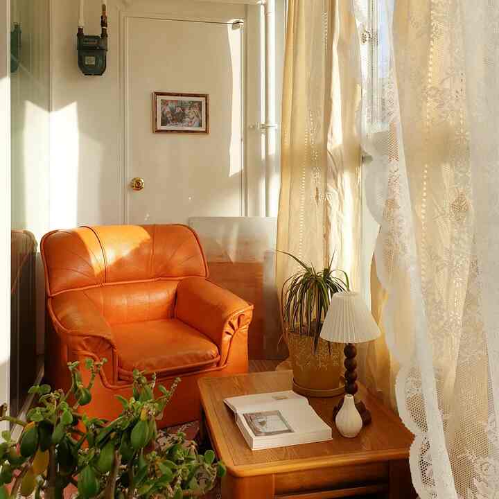 Warm beige and orange toned veranda space featuring an orange armchair, wooden coffee table, and plants in a cozy home cafe setting