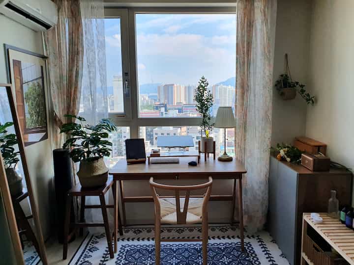 Natural brown and white toned home office space with desk and stool by window, plants adding cozy atmosphere