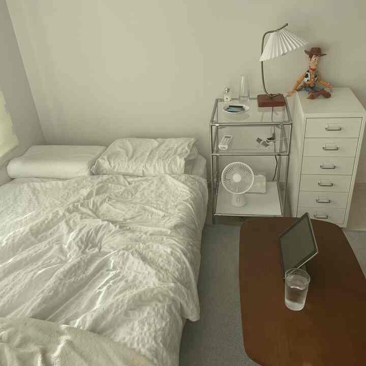 A simple and cozy bedroom in white and gray tones featuring a bed, dresser, and wooden table