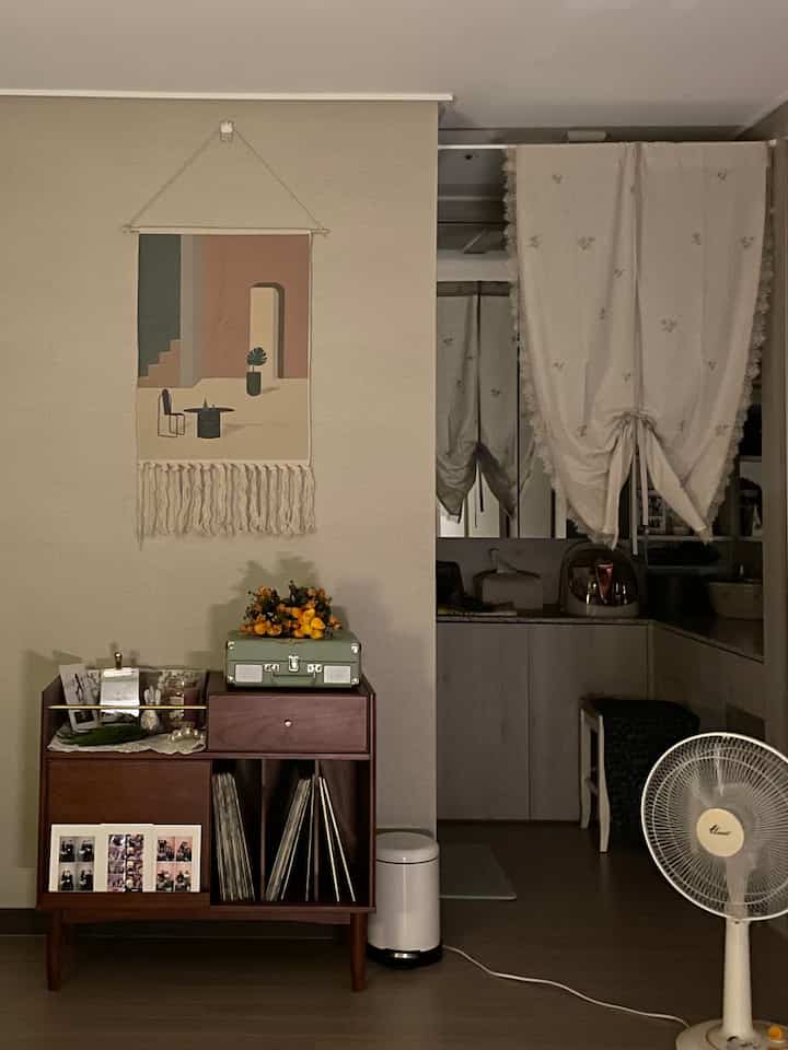 Beige and white toned bedroom featuring curtains, retro cabinet with turntable, and fabric poster creating a cozy atmosphere