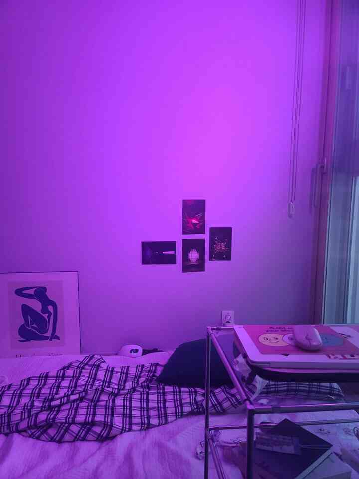 紫色の照明が灯る寝室、ネイビーチェックの寝具と壁の額縁アート、モバイルテーブルが配置された雰囲気のあるワンルーム
