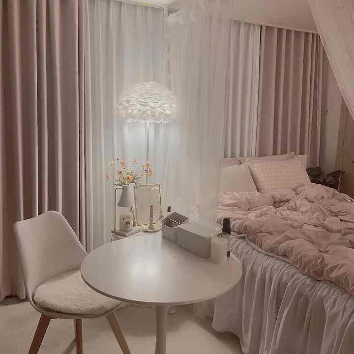 柔らかな白とピンクのトーンのワンルーム寝室、ベッドと木製の椅子が配置された雰囲気のある空間