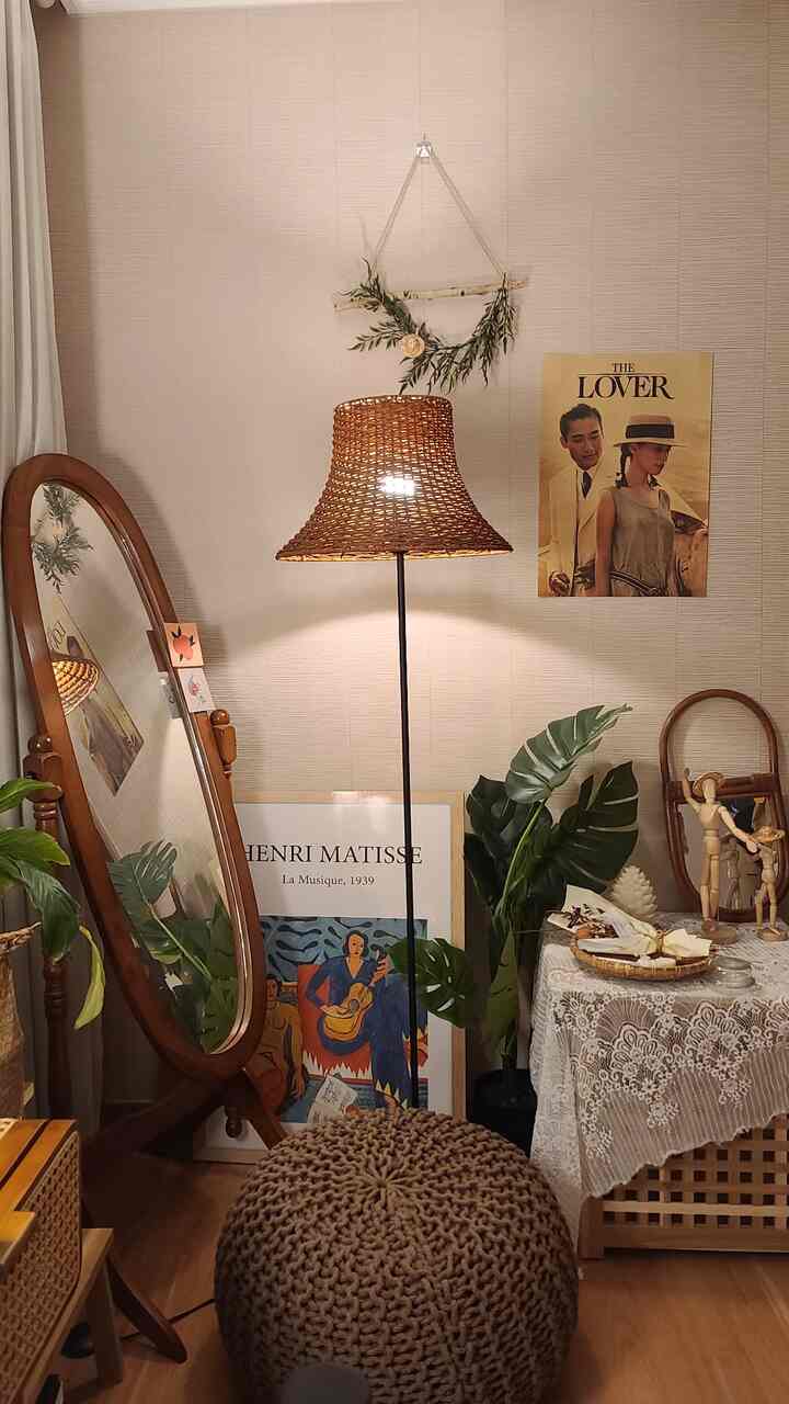 Beige-walled bedroom with rattan floor lamp, standing mirror, and plants creating a warm natural interior