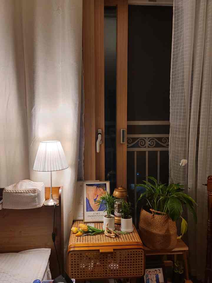Natural color toned bedroom featuring a rattan nightstand with plants and blackout curtains creating a cozy atmosphere