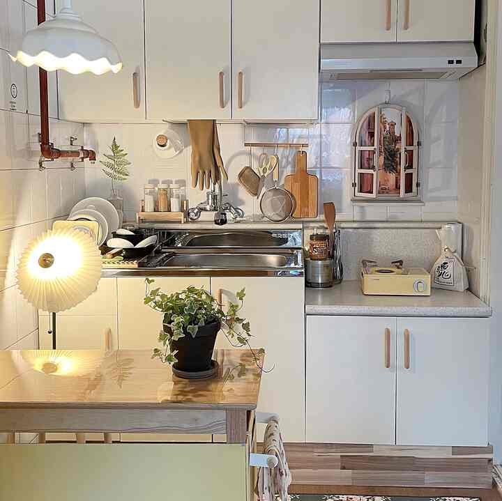 Compact kitchen in natural wood tones and white featuring a wooden dining table and hanging kitchen utensils, creating a cozy atmosphere