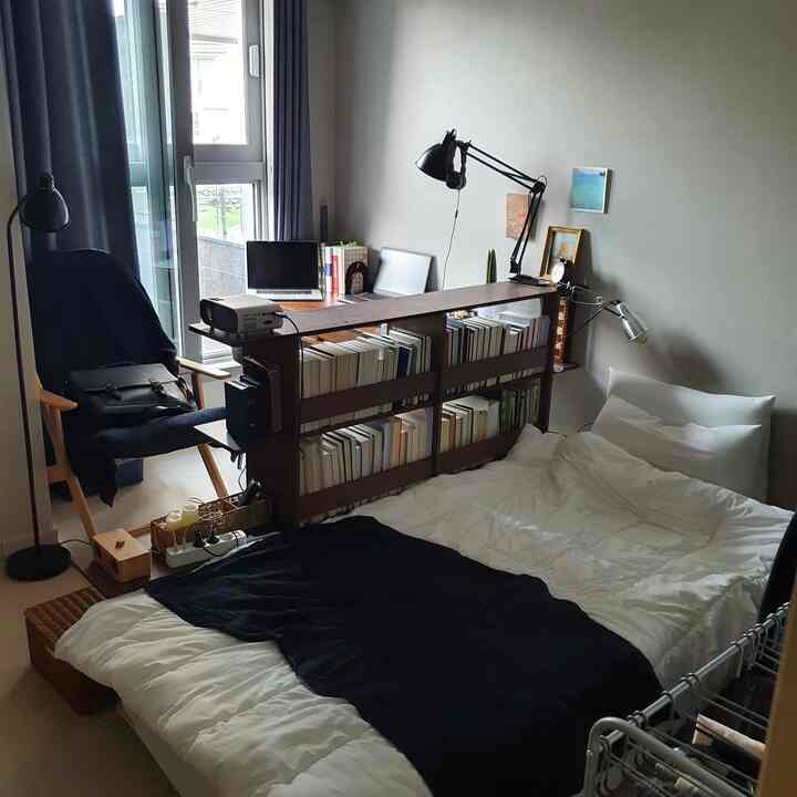 ホワイトとブラックのトーンでまとめられたワンルームの寝室兼ホームオフィス。棚や机、ベッドが整然と配置された落ち着いたインテリア