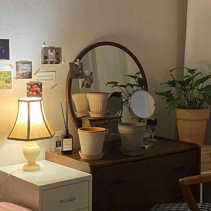 温かみのあるナチュラルカラーの木製チェストとテラコッタ鉢、植物が配置されたヴィンテージ風の寝室の化粧台空間
