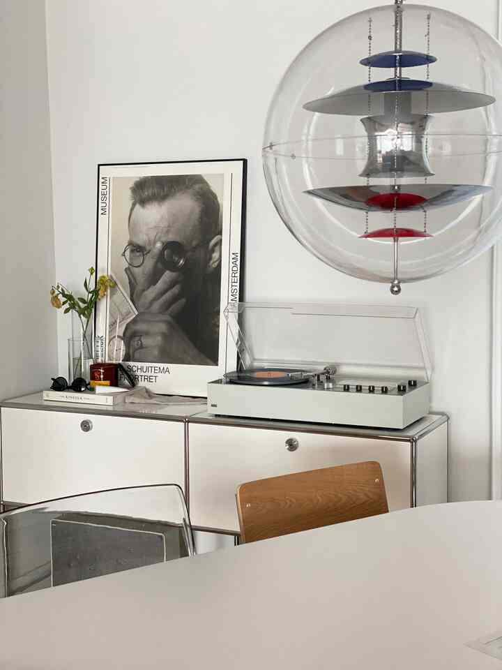 A white and wood tone living room featuring a system cabinet with framed art and record player, large spherical pendant light, exuding a minimal and modern atmosphere