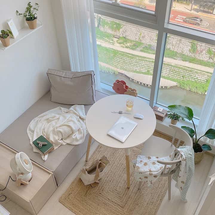 White and beige studio apartment space featuring a round dining table and sofa with natural light creating a bright and cozy atmosphere