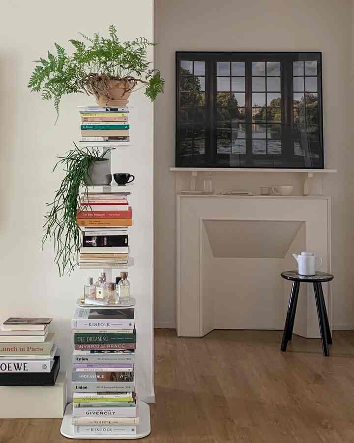 白と茶色のトーンのリビングルーム、スタックされた本棚と植物が配されたモダンでミニマルなインテリア