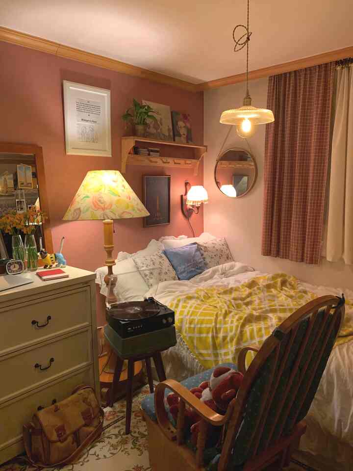Cozy bedroom in warm brown and pink tones featuring a turntable on stool, nightstand, wall sconce, and a yellow blanket for relaxing ambiance