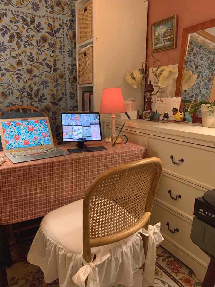 暖かいベージュとブラウンの色調の寝室兼ホームオフィス、長いデスクにノートパソコンとタブレット、ヴィンテージ風の小物が並ぶ雰囲気のあるインテリア