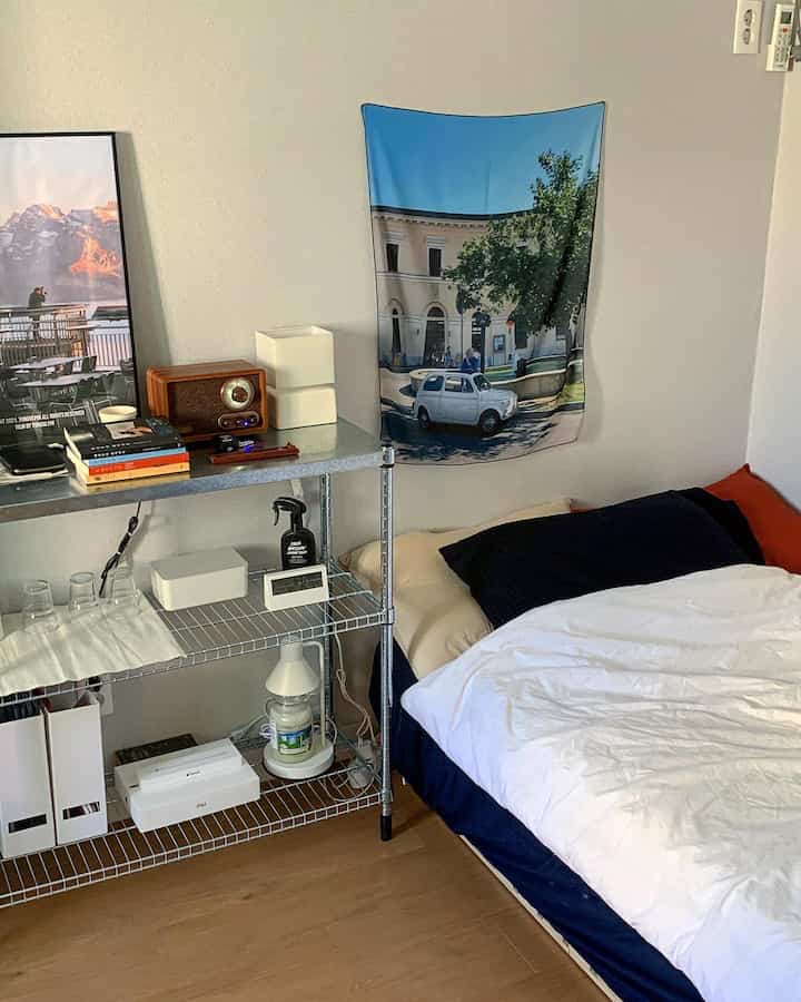 Natural-toned studio bedroom with navy, white, and wood elements, featuring shelves with posters and decor items
