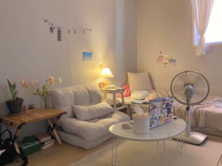 Warm beige natural-toned studio living room featuring low sofa, bed, stool, and round table creating cozy atmosphere