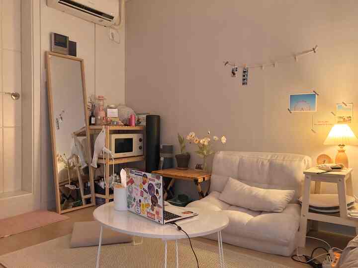 A small living room with a white and wood tone palette, featuring a simple sofa, round coffee table, and a warm table lamp creating cozy ambiance