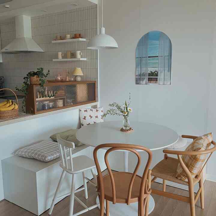 A cozy white and wood tone kitchen dining room featuring a round table, bench seating, and an arched poster.
