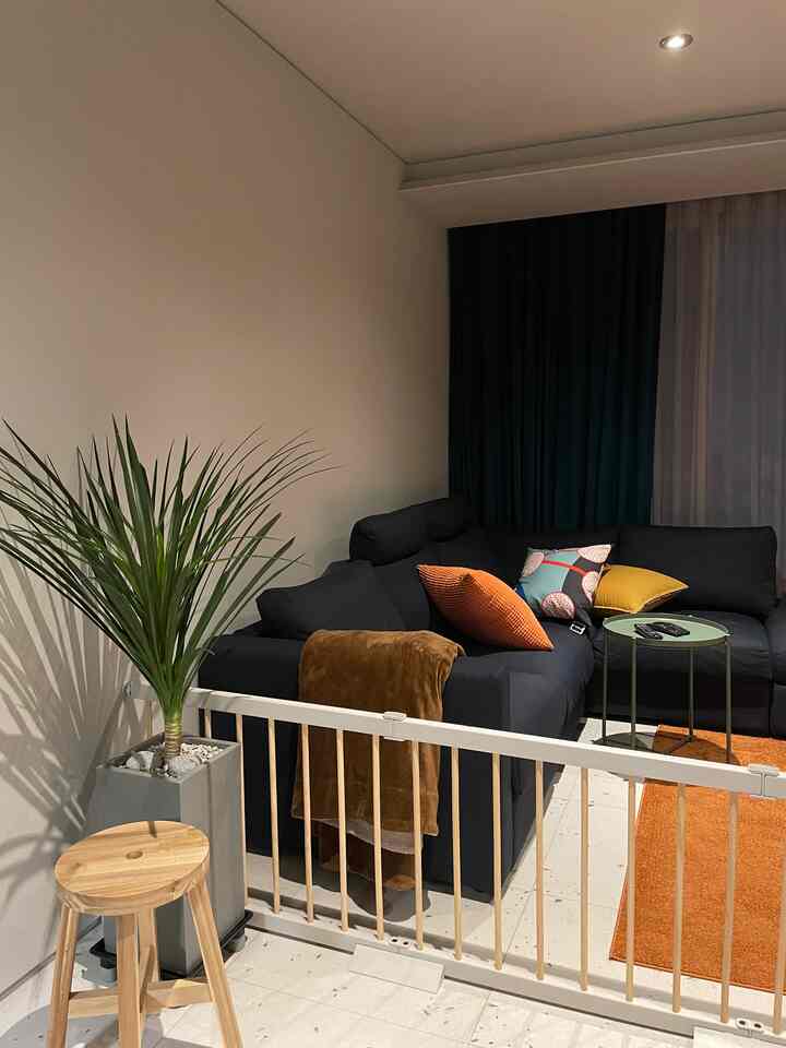 Living room in black and orange tones featuring dark blackout curtains, sectional sofa, wooden stool, and a plant creating a warm atmosphere