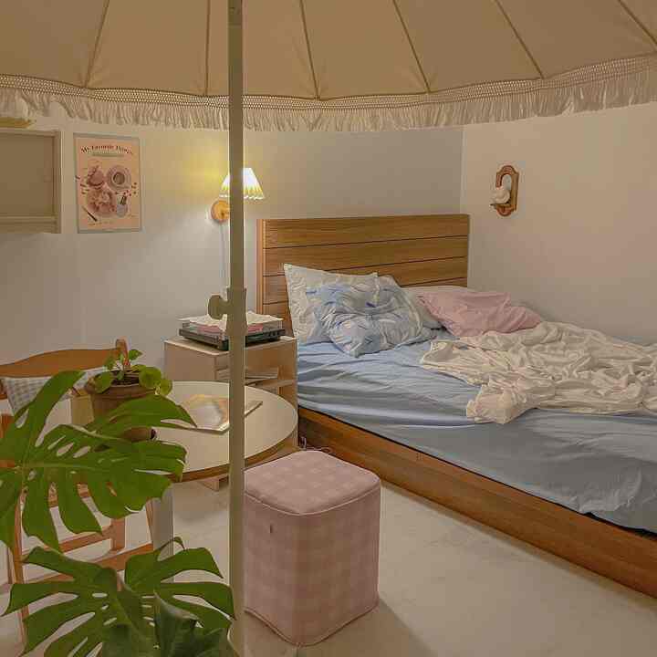 A natural beige-tone and white-walled bedroom featuring a round table and pink stool creating a cozy and simple interior atmosphere