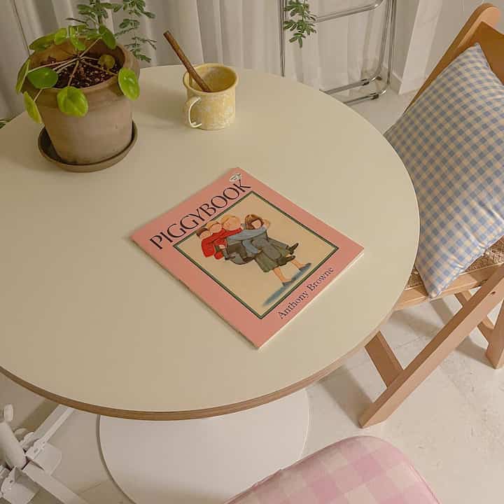 ベージュとホワイトの色調の子供部屋、丸いダイニングテーブルにホーローマグとチェック柄クッションが配置された温かみのあるインテリア