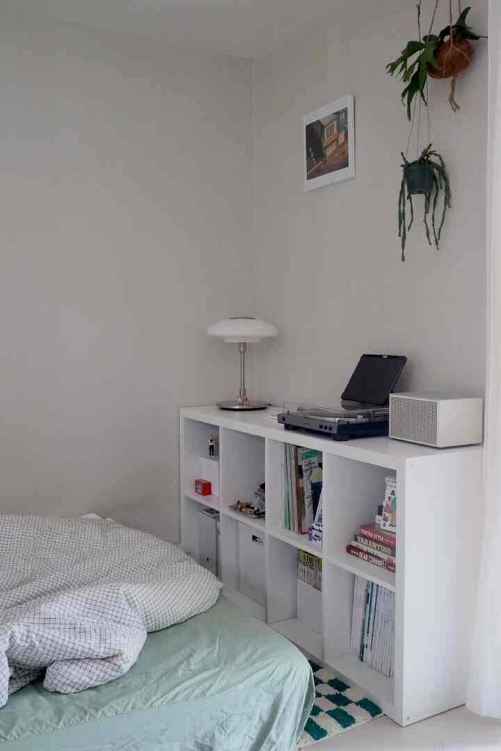 ホワイトと淡いグリーン調のミニマルでナチュラルな寝室、本棚、照明、ハンギングプランツが配置された空間