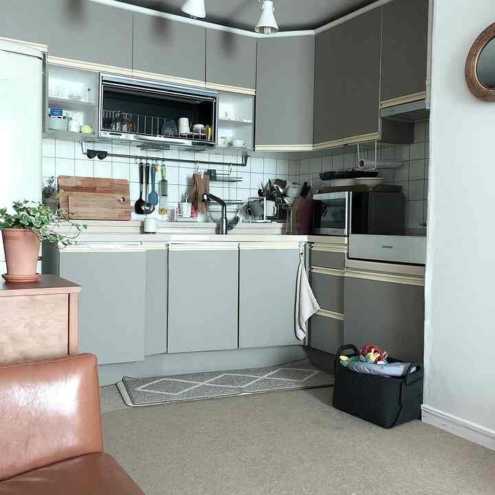 Compact kitchen space with gray cabinets and brown leather sofa, featuring organized setup and practical interior design