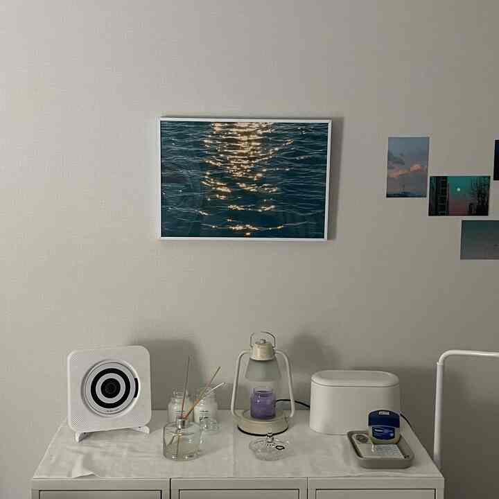 A simple white and natural toned room featuring a dresser with picture frame, candle, and diffuser in a neat setup