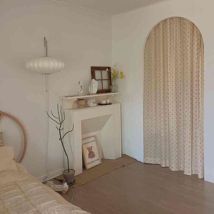 A beige and natural tone bedroom featuring an arched doorway with patterned curtain, bed, and a decorative fireplace creating a cozy atmosphere