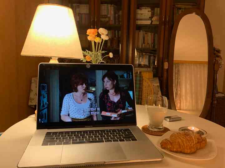 Cozy small living space in warm brown and white tones featuring a full-length mirror, bookshelf, and table with a laptop, croissant, and glass of milk