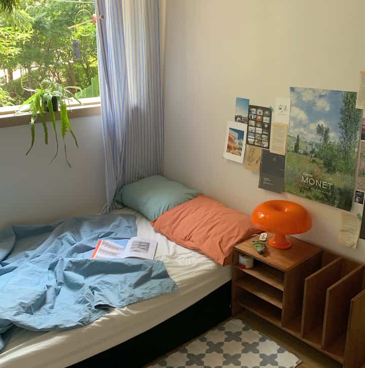 A small bedroom in white and blue tones featuring an orange lamp and wood-tone side table, creating a cozy atmosphere