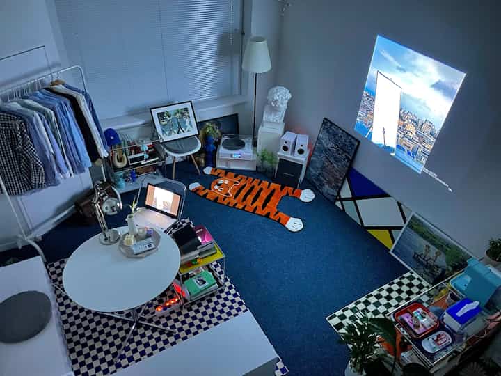 Blue flooring and white furniture in a single household workspace with a projector and LP turntable creating an atmospheric room