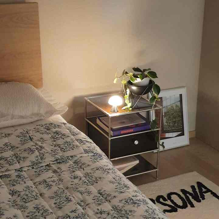 ホワイトトーンの寝室、モジュラー金属製のナイトスタンドに小さなLEDランプと植物が配置された落ち着いた空間