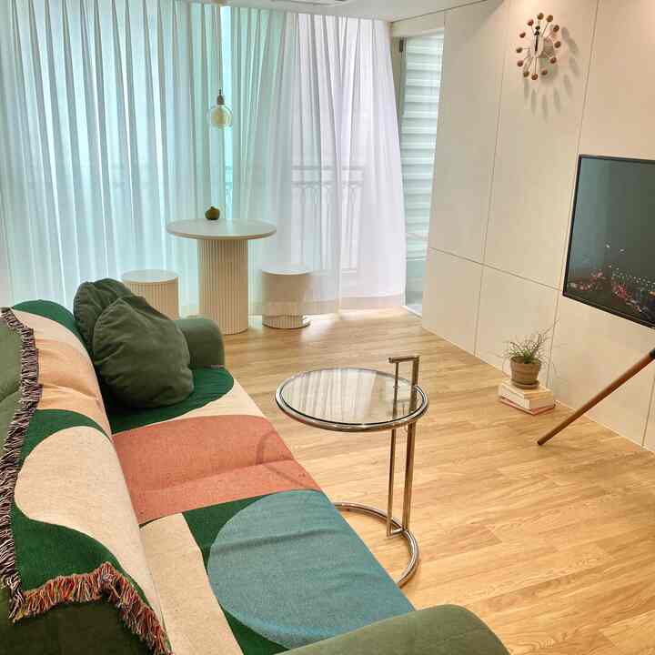 Natural wood tone flooring and white curtains in living room featuring green sofa and coffee table in a simple setting