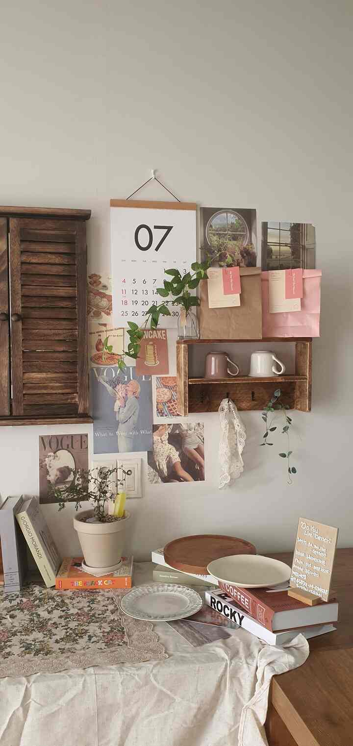 Cozy kitchen space with beige and wood tones featuring vintage wood shelves, artificial vines, and a floral tablecloth creating a warm atmosphere