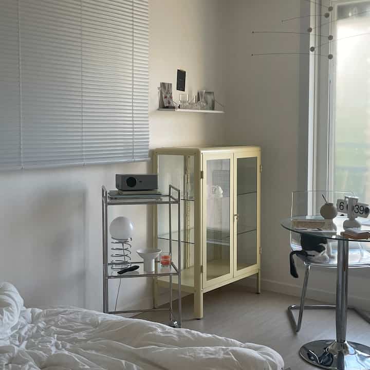 Natural toned living room featuring butter-colored cabinet and transparent chair with a cat, reflecting clean minimal interior