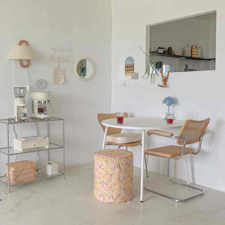 White-toned space with natural wood dining chairs and table featuring a partition wall separating kitchen and living area
