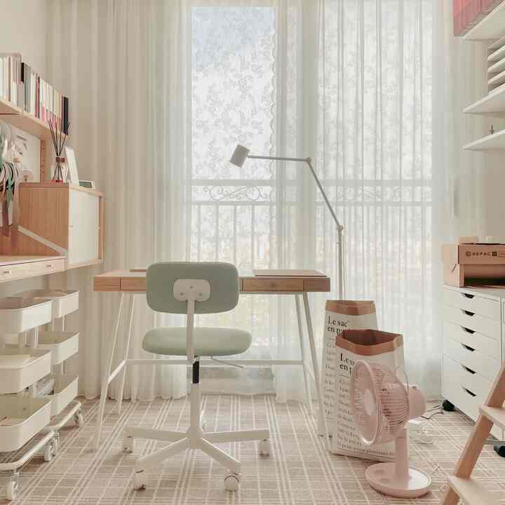 Bright white and wood tone small home office with curtains, neat desk and office chair creating a cozy workspace