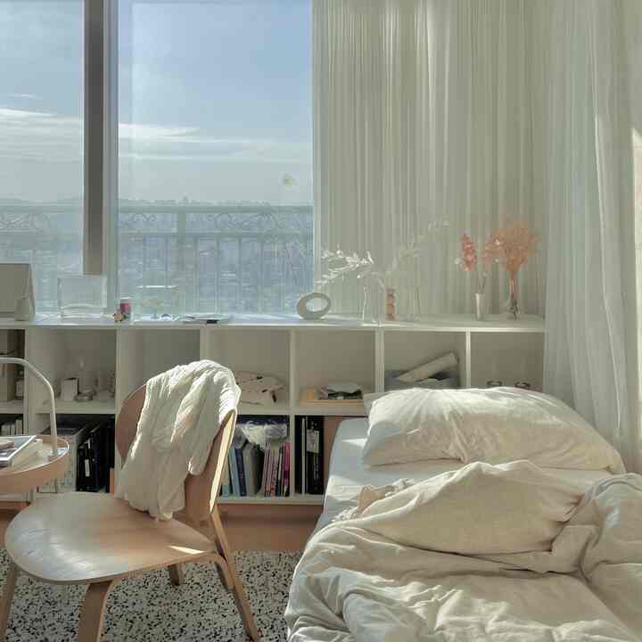 A compact bedroom in beige and ivory tones featuring natural light through large windows and wooden chairs, creating a cozy atmosphere