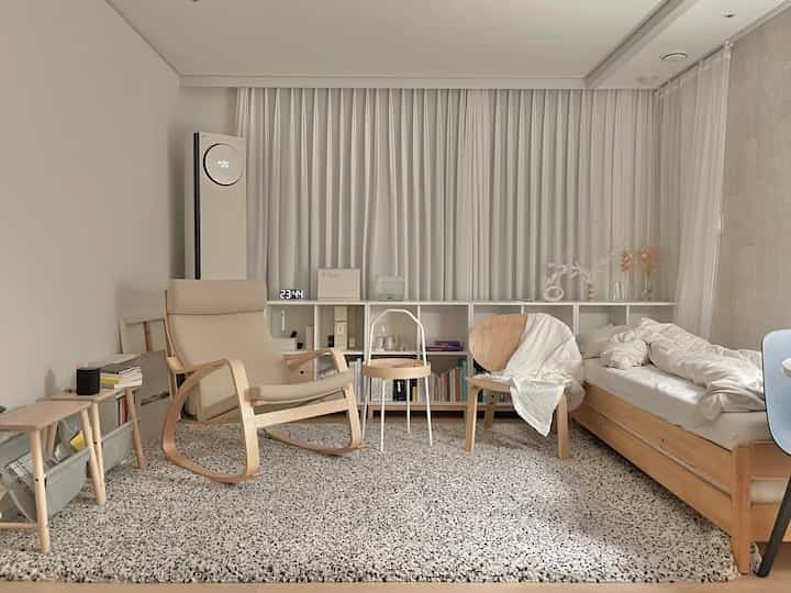 White curtains as backdrop with natural wood-tone furniture arranged in a simple modern single household living space