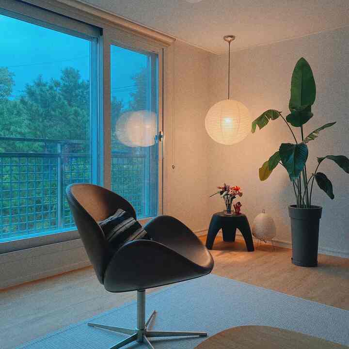 Light brown wood floor and white walls in living room featuring dark brown armchair, stool, large plant, and pendant light creating a cozy atmosphere